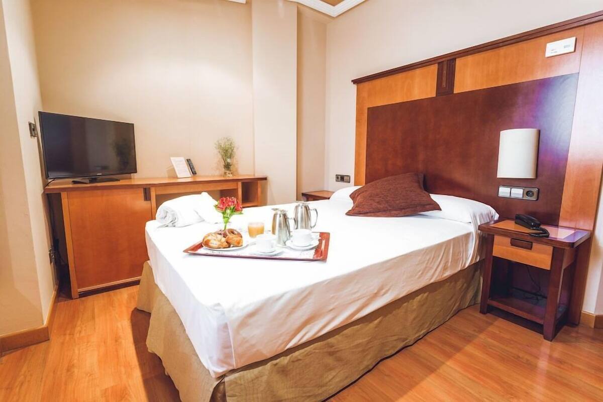 A hotel room with a bed, bedside table, TV, and a breakfast tray.