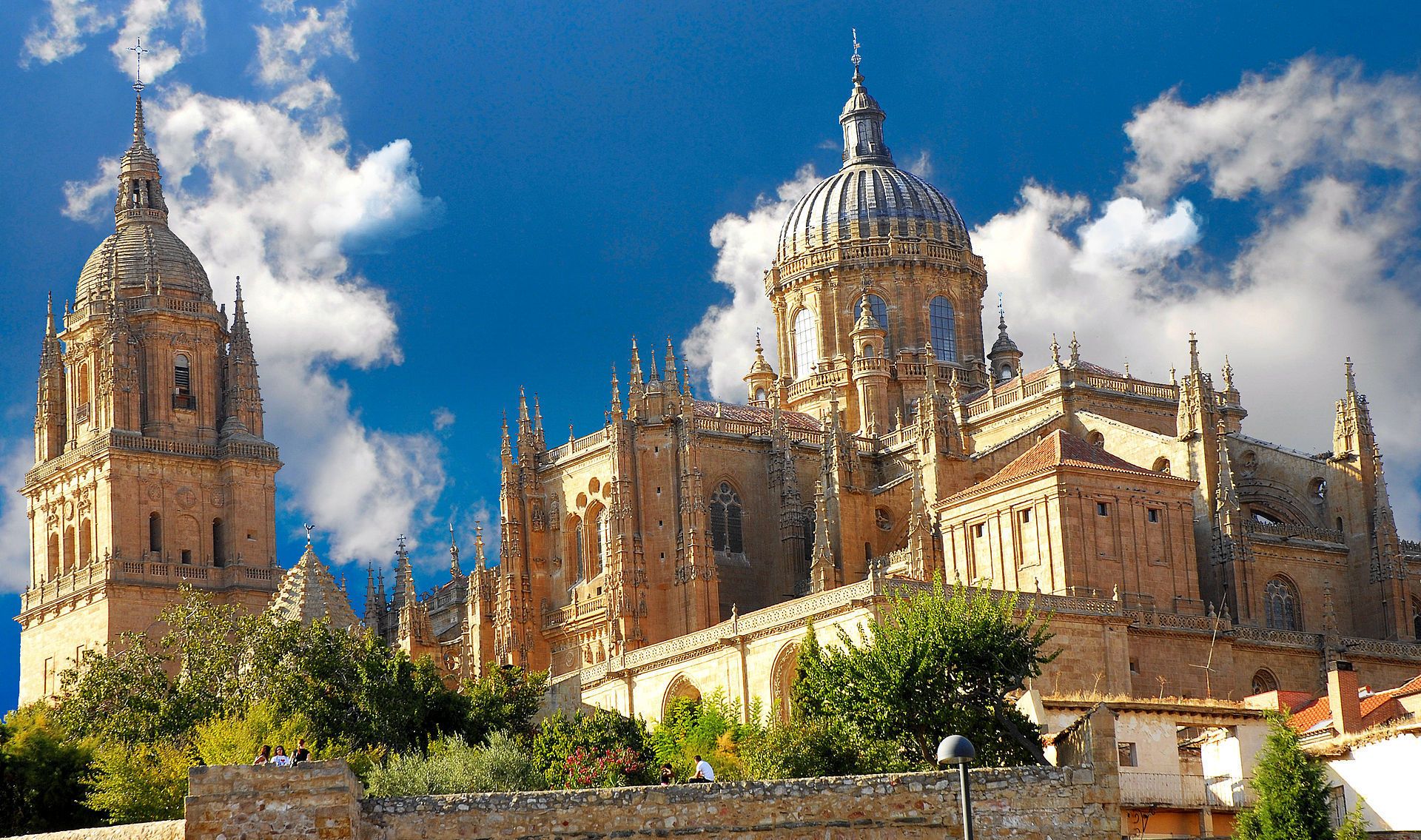 A historic cathedral with two prominent towers and a large dome, surrounded by lush greenery and a clear blue sky.