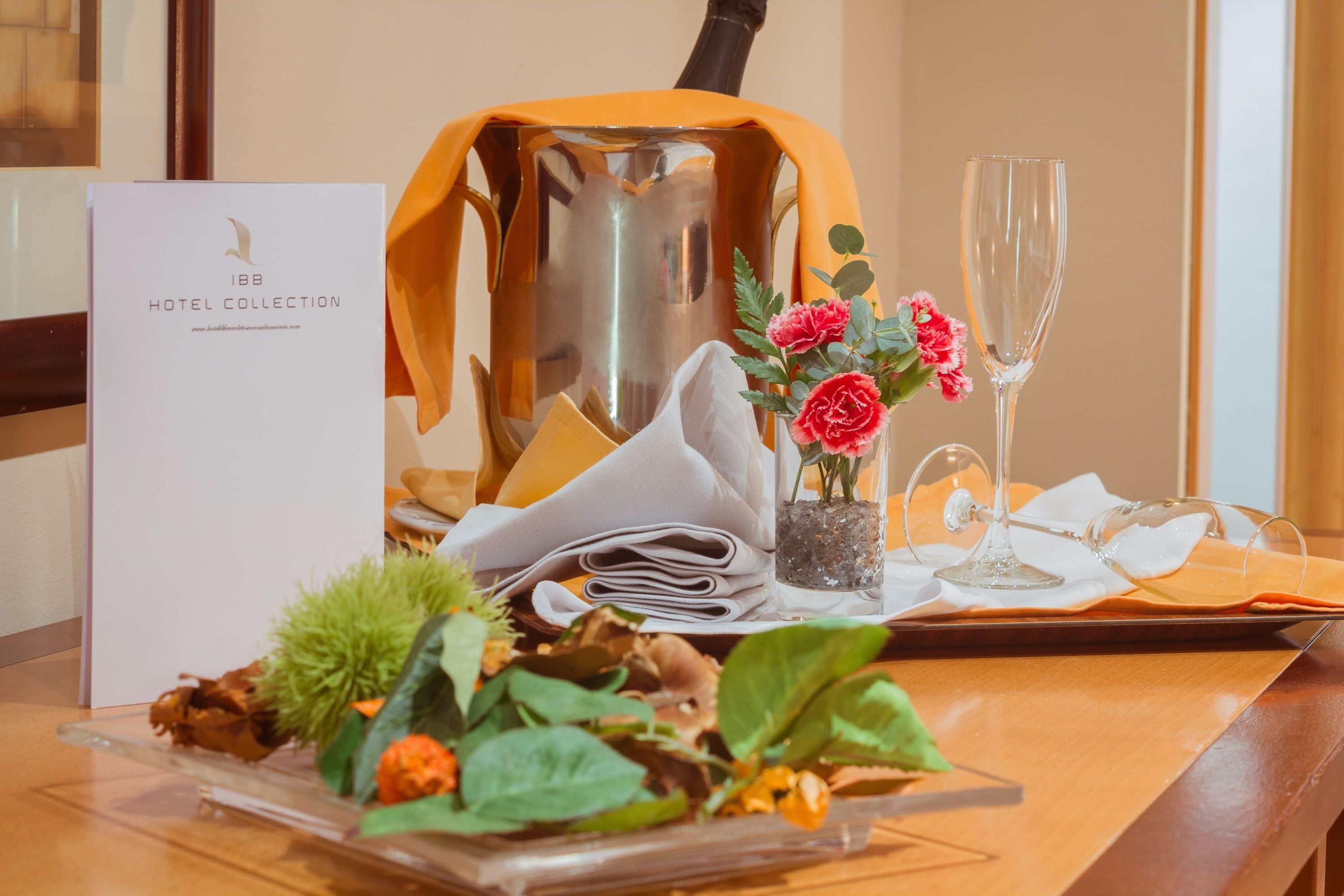 A table set with a menu, a vase with flowers, a glass of champagne, and a decorative pitcher.