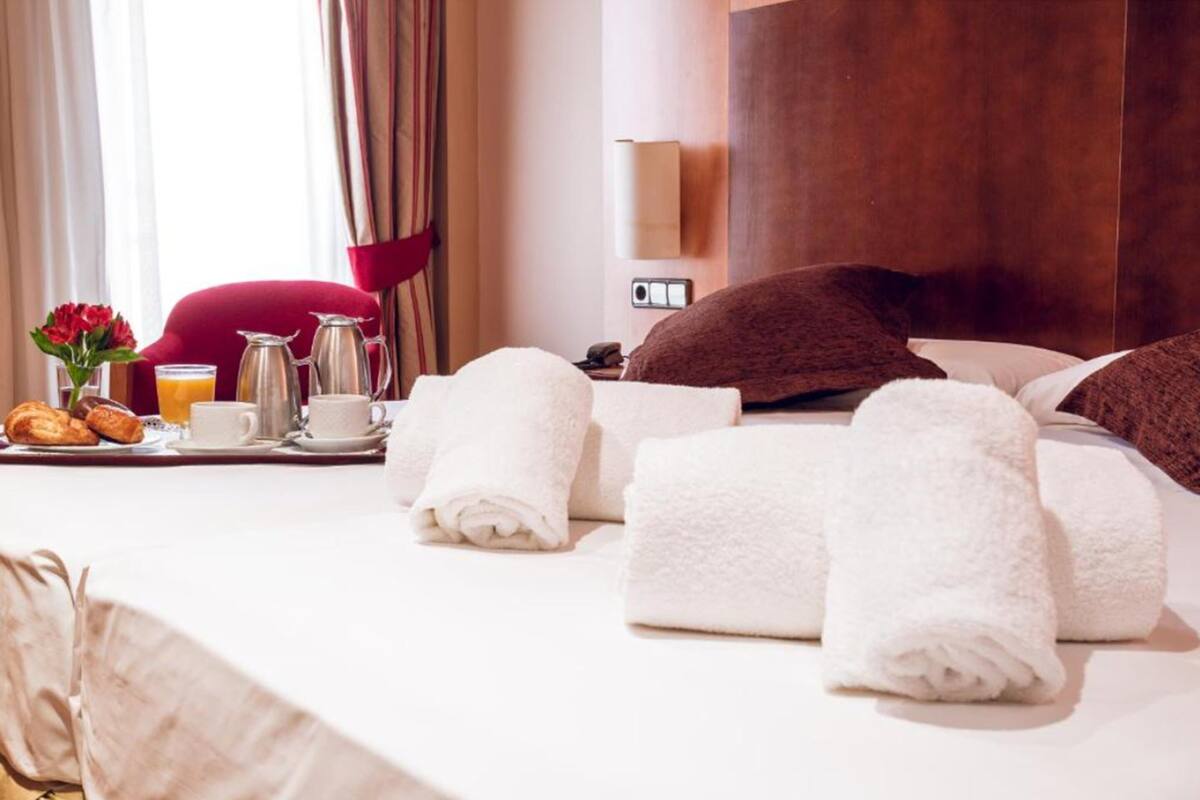 A neatly made bed with white towels, a tray with croissants, a coffee pot, and a glass of orange juice.
