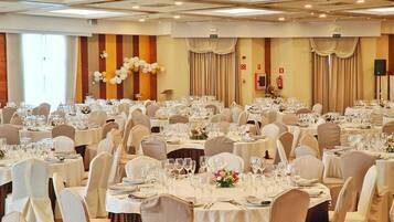 Un salón de banquetes con mesas redondas dispuestas para comer, sillas blancas e iluminación empotrada en el techo.