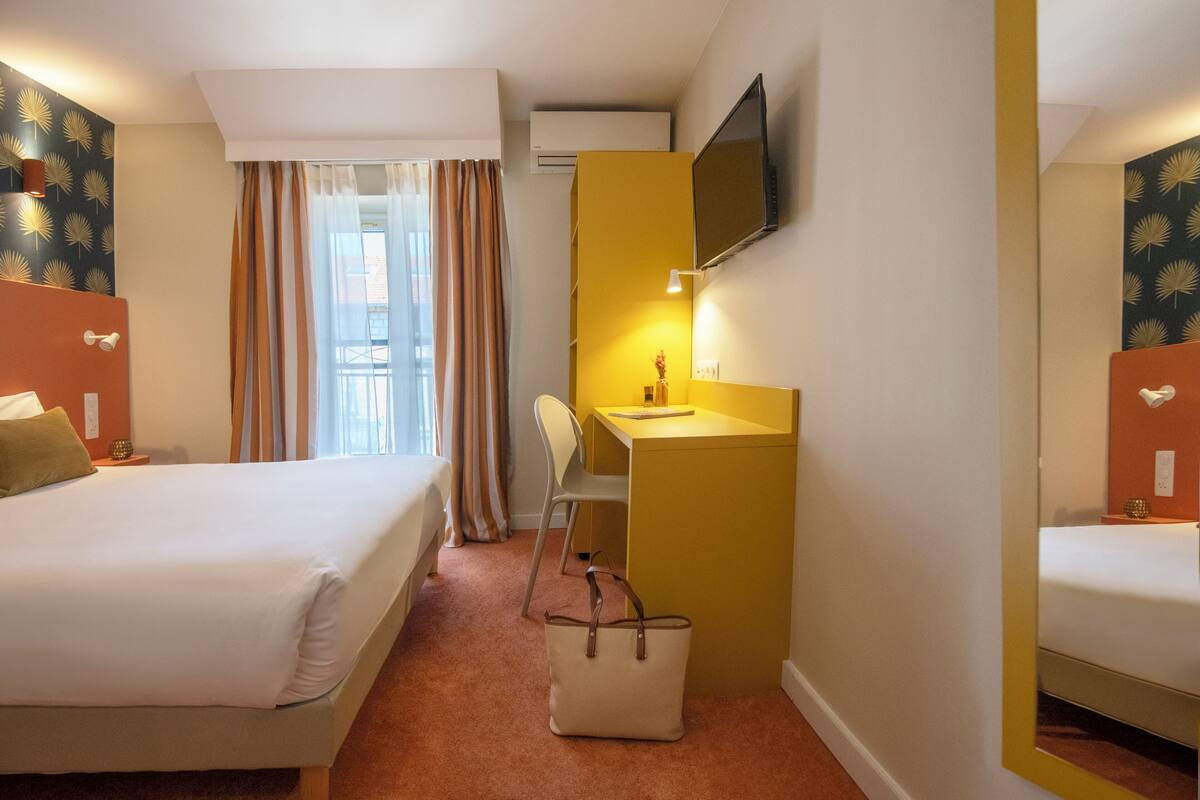 A hotel room with a bed, a desk, a chair, a TV, and a window with curtains.