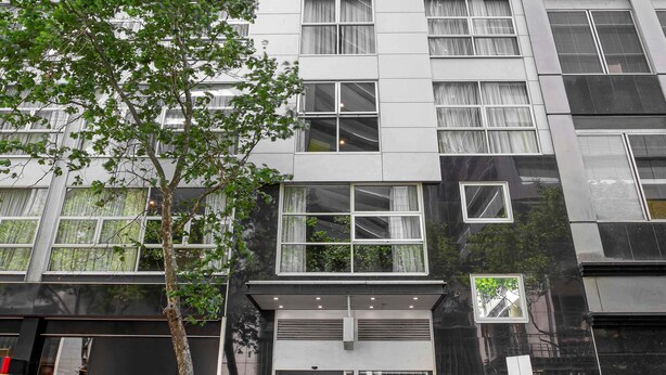 Un bâtiment moderne doté de nombreuses fenêtres, avec un arbre devant et une enseigne indiquant « mantra 100 ».