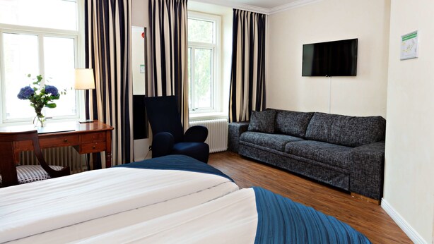 Une chambre d’hôtel équipée d’un lit, d’un bureau, d’une chaise, d’un canapé et d’un téléviseur fixé au mur.