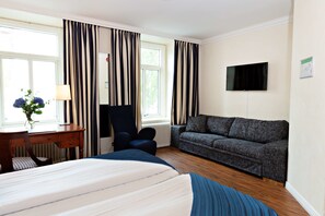 Ein Hotelzimmer mit Bett, Schreibtisch, Stuhl, einer Sitzecke und einem Fernseher an der Wand.
