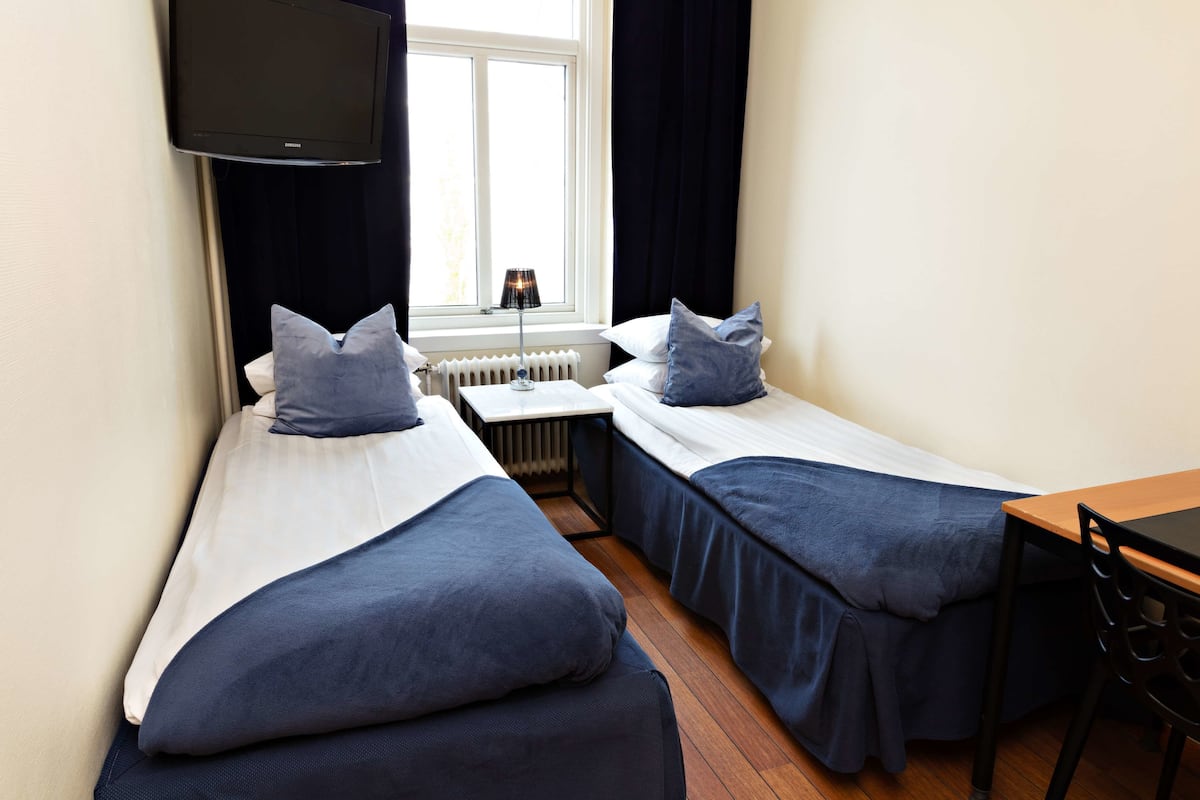 A twin room with two single beds, a table, a chair, a TV, and a window with curtains.