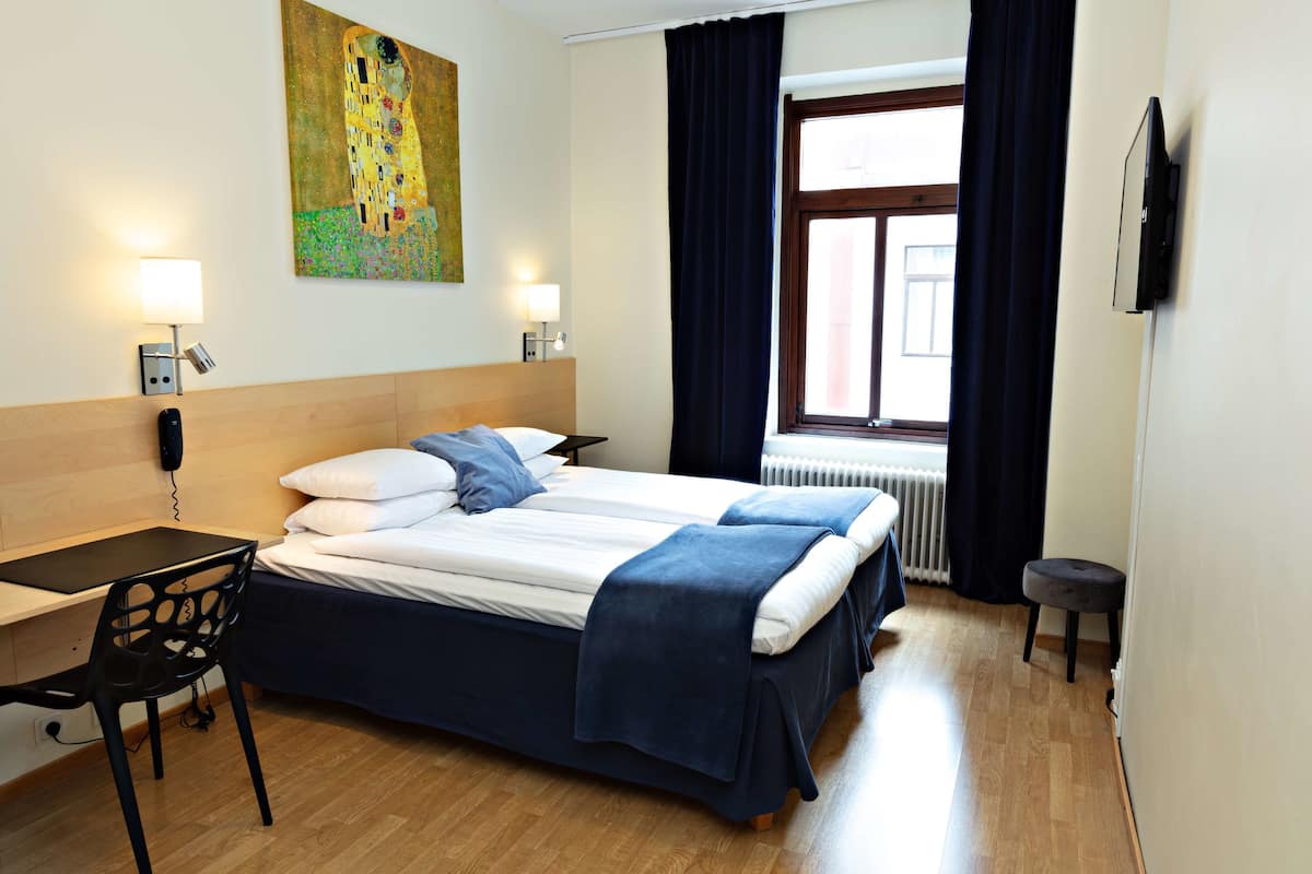 A hotel room with a bed, desk, chair, and a painting on the wall.