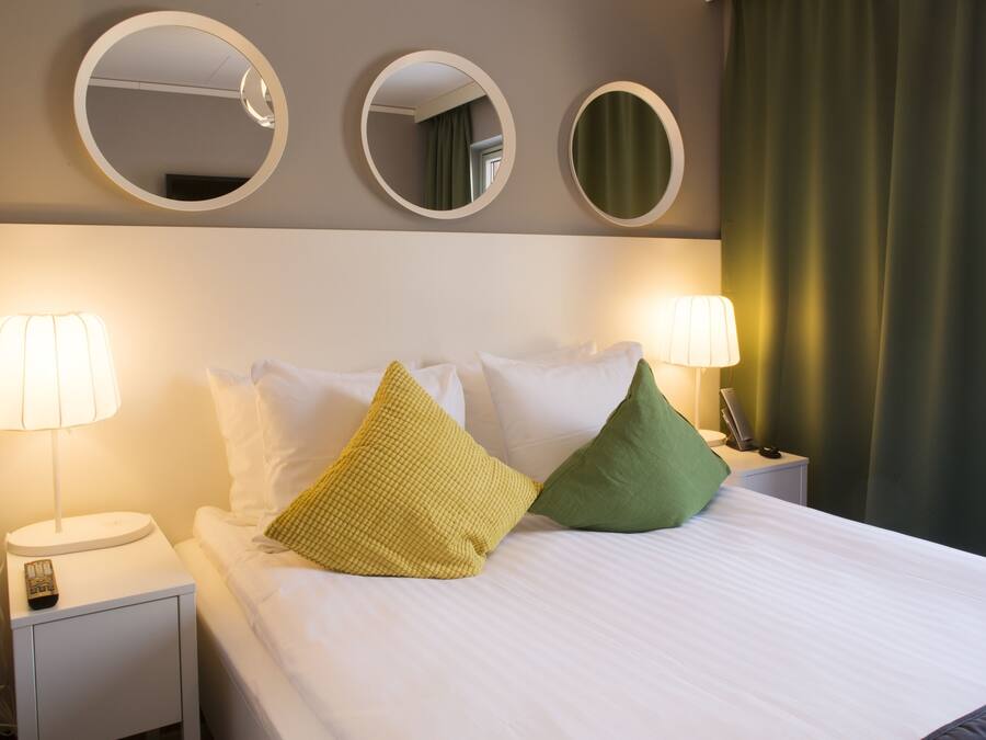 A neatly made bed with white linens, two bedside lamps, and three round mirrors on the wall above.