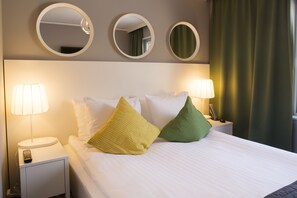 A neatly made bed with white linens, two bedside lamps, and three round mirrors on the wall above.