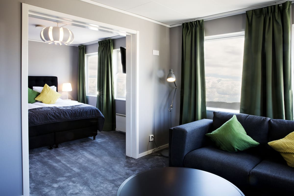 Una habitación de hotel moderna con una cama, un sofá, una mesa y vistas al cielo.