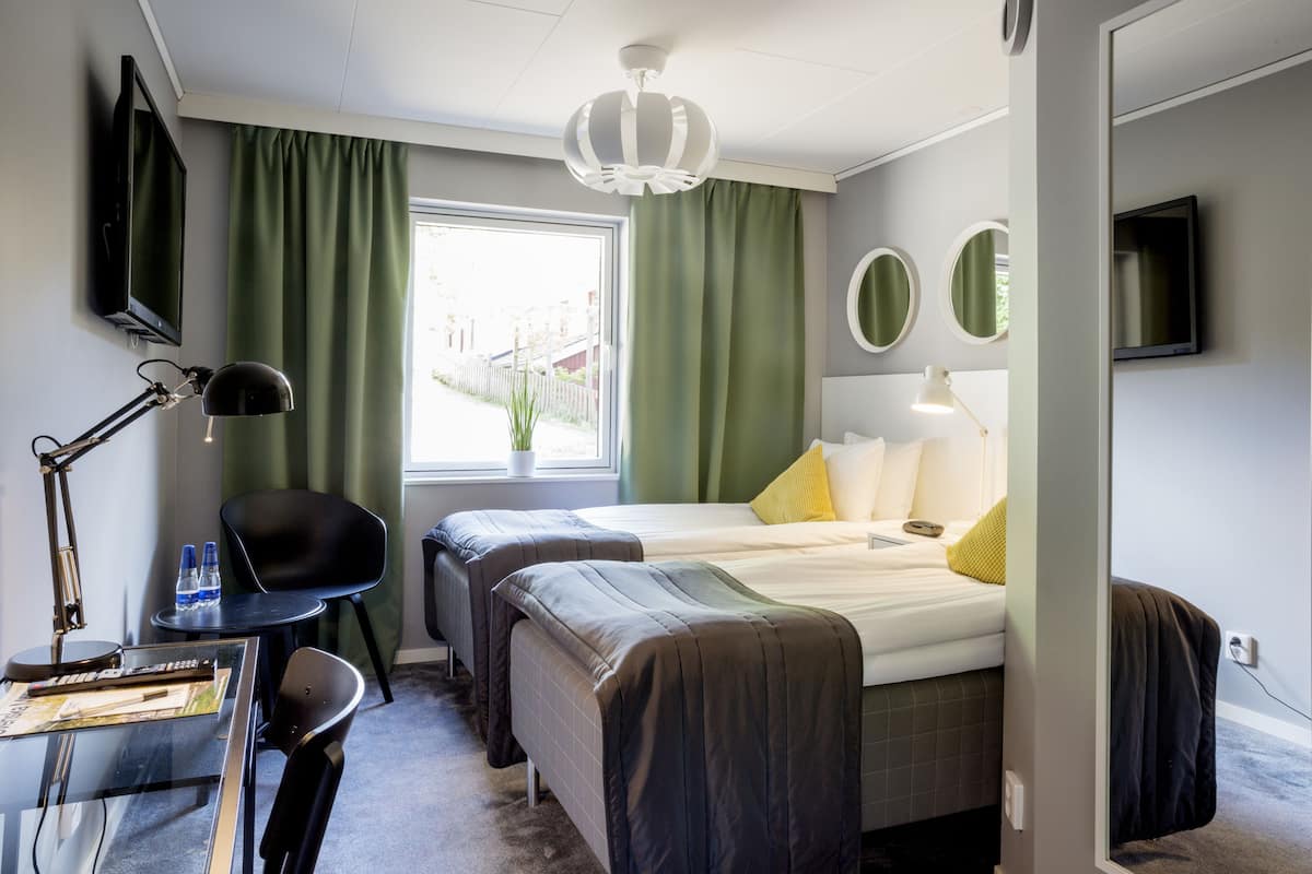 Habitación de hotel con dos camas, un escritorio con silla, televisión y ventana con cortinas.