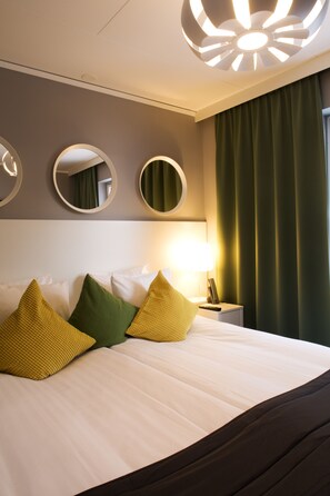 A hotel room with a large bed, a nightstand with a lamp, and three wall-mounted mirrors.