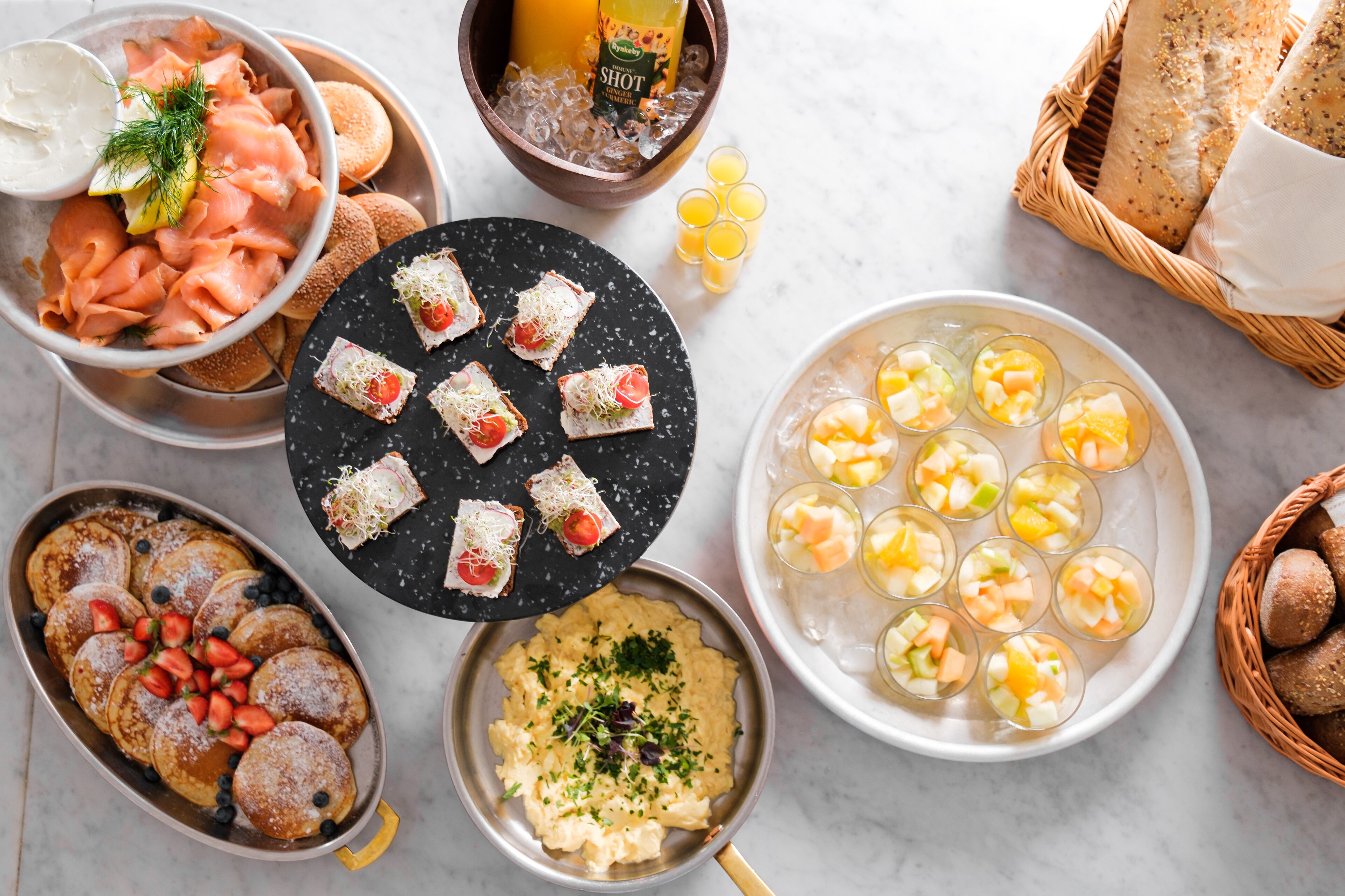 Diversos alimentos, incluindo panquecas, salmão defumado e copos de fruta.