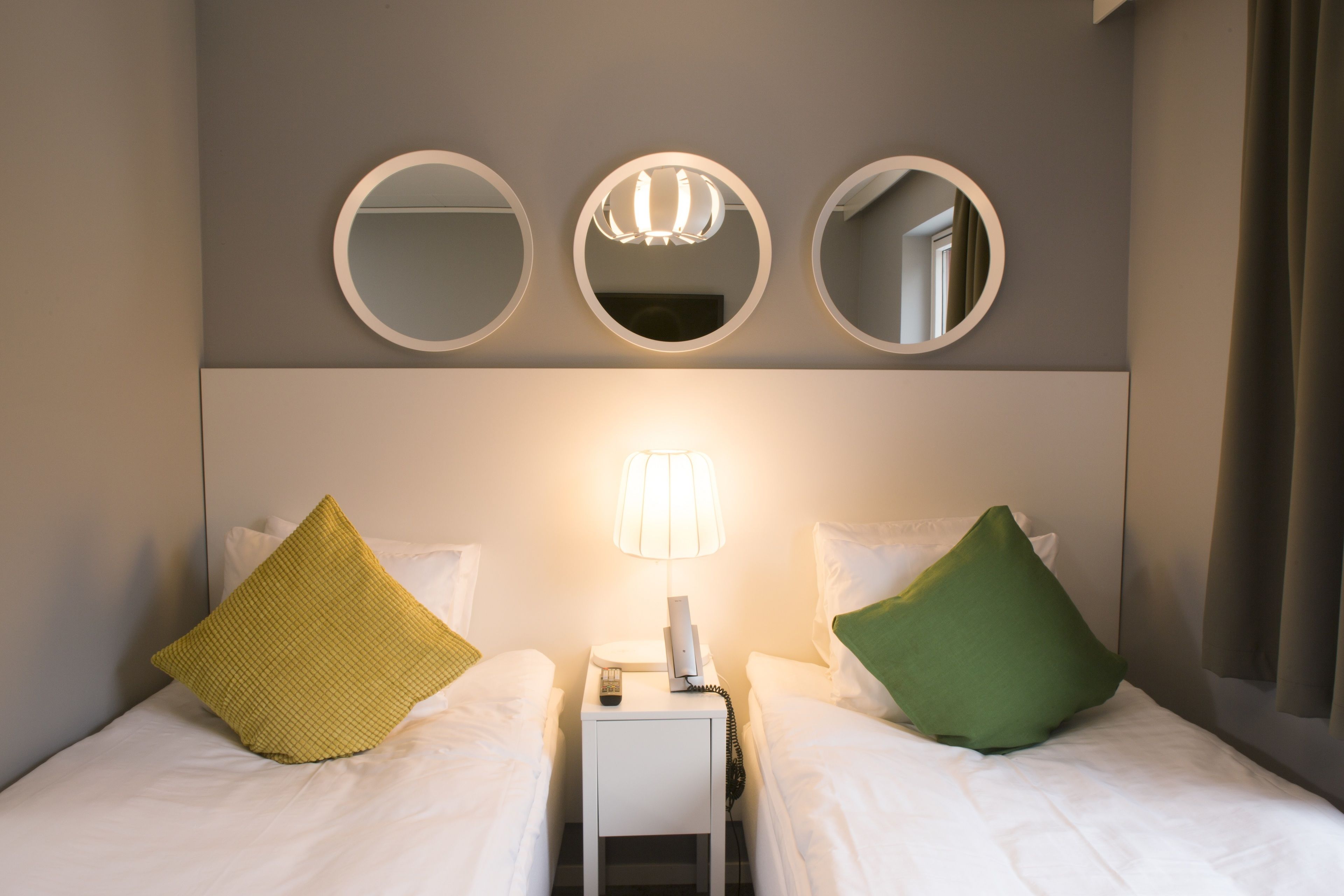 A hotel room with two beds, a nightstand with a lamp, and three wall-mounted mirrors.