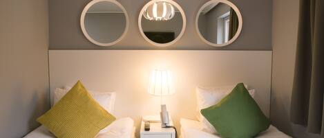 A hotel room with two beds, a nightstand with a lamp, and three wall-mounted mirrors.