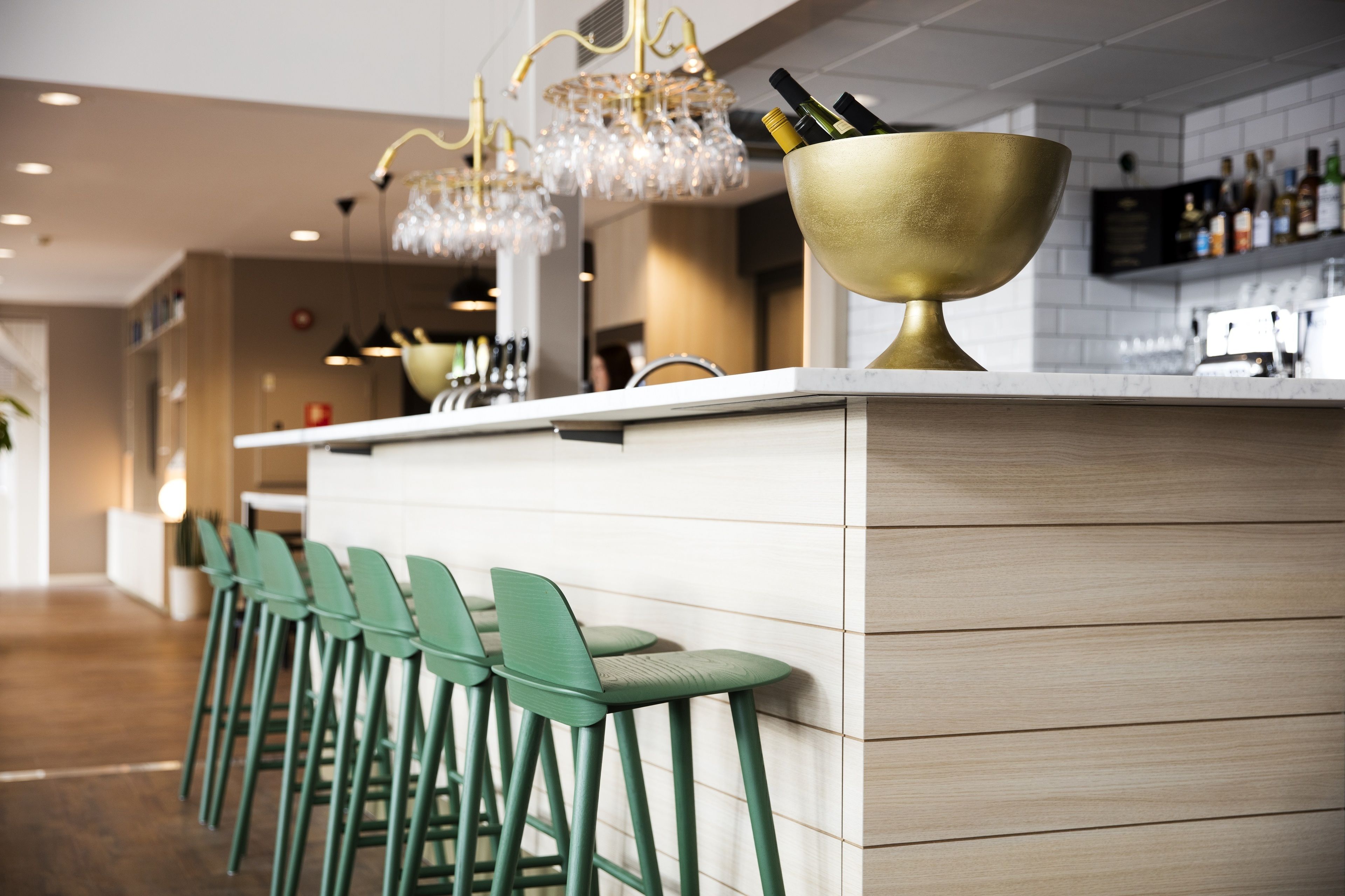 Una cocina moderna con barra, taburetes verdes y un cuenco dorado grande sobre la encimera.