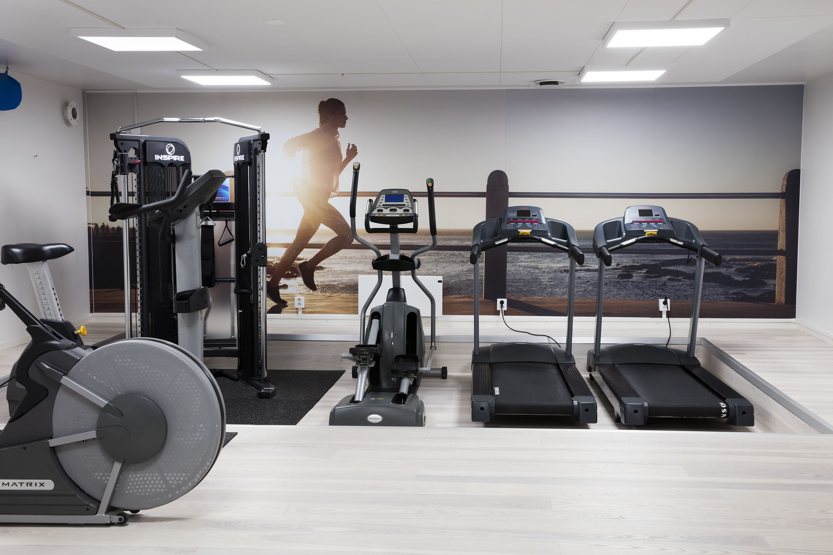 A gym with cardio equipment, a rowing machine, and a wall mural of a runner.