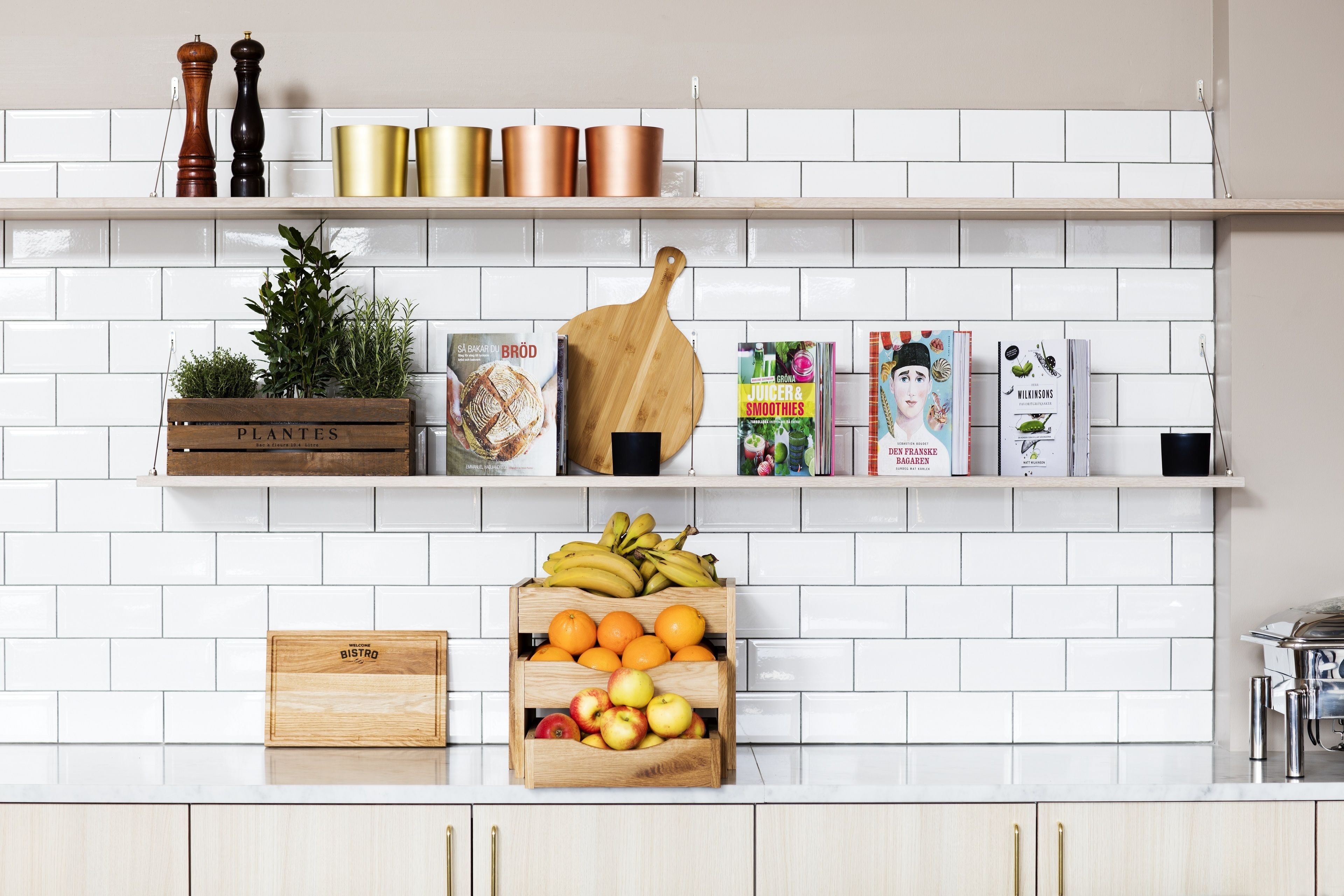 Una cocina con salpicadero de azulejos blancos, estantes de madera y diversos utensilios de cocina.