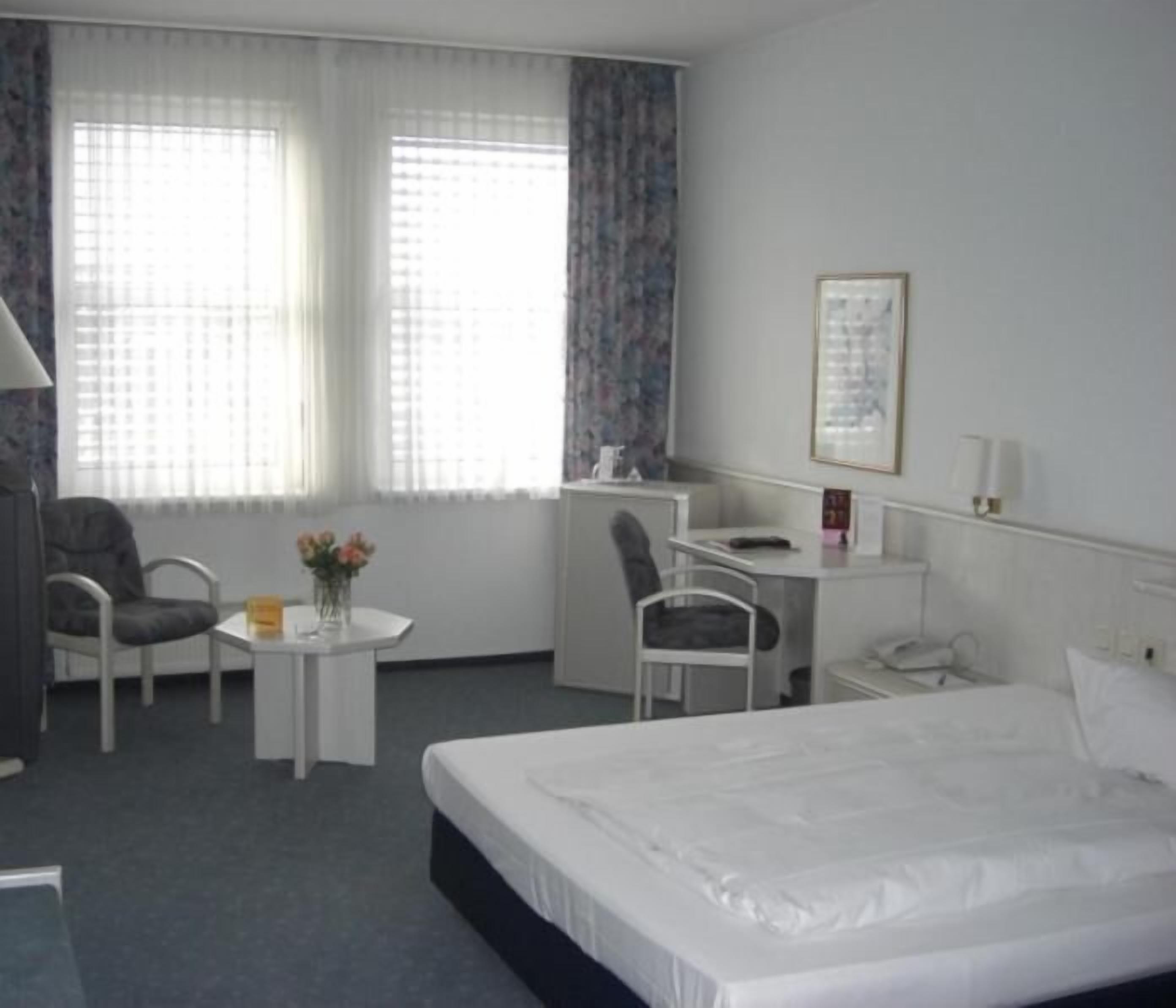 A hotel room with a bed, a desk, a chair, and a small table with flowers.