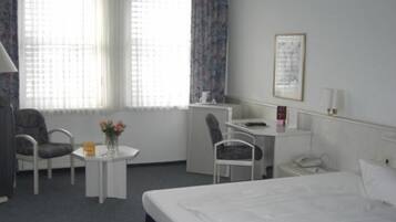 A hotel room with a bed, a desk, a chair, and a small table with flowers.