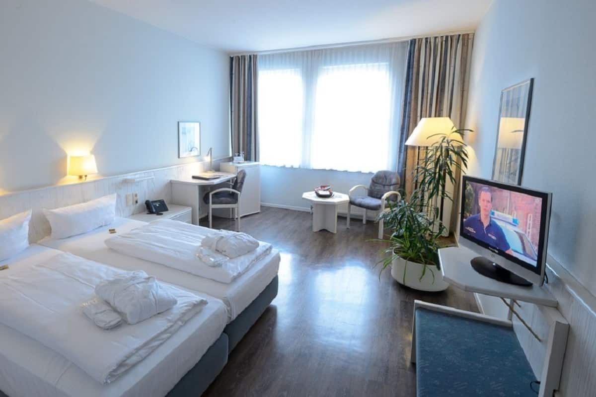 A hotel room with two beds, a desk, a chair, a TV, and a potted plant.
