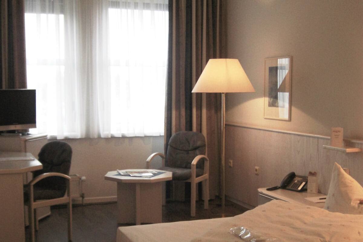 A hotel room with a bed, a desk with a chair, a lamp, a television, and a telephone.