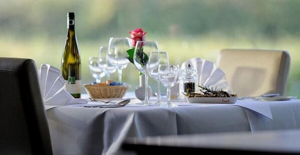 A dining table set with wine glasses, a bottle of wine, a rose, and a basket of fruits. - Euro Park Hotel Hennef (Hennef)