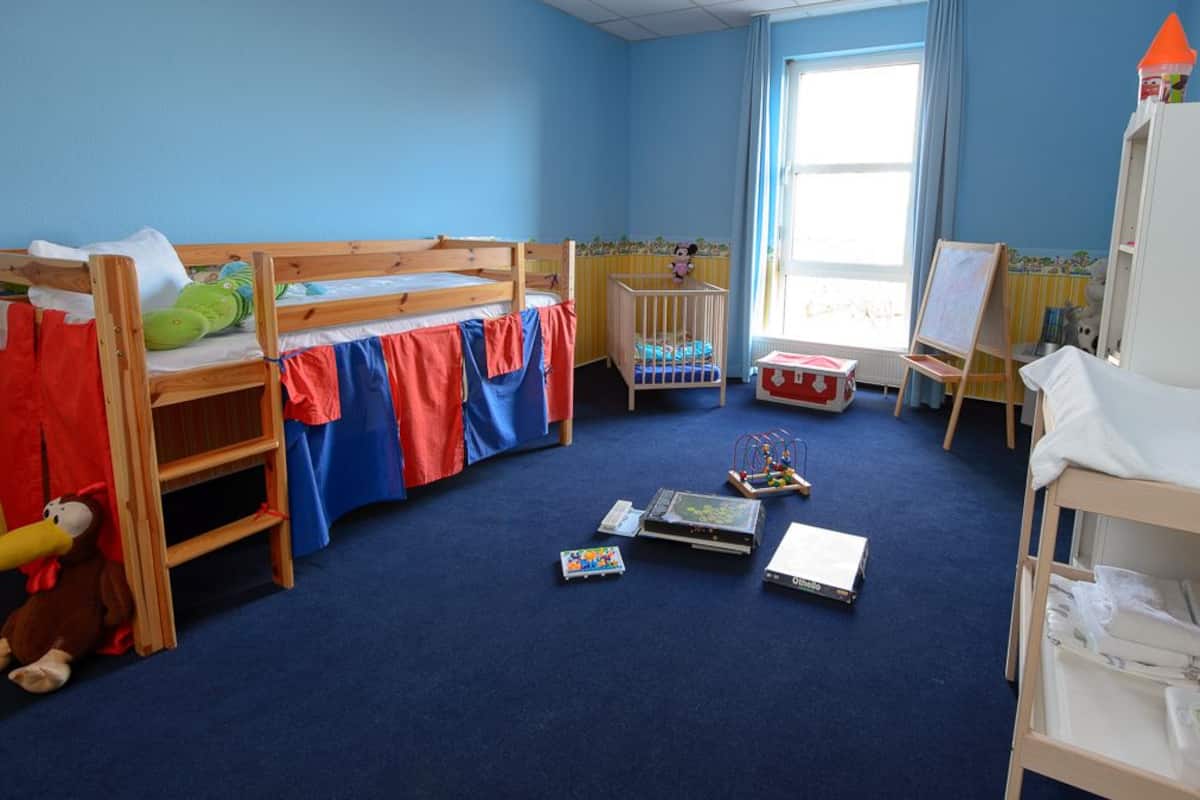 A children's room with bunk beds, a crib, a play area with toys, and a window with curtains.