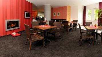 Una habitación de hotel con chimenea, varias mesas de comedor, sillas de mimbre y piso cubierto de alfombra.