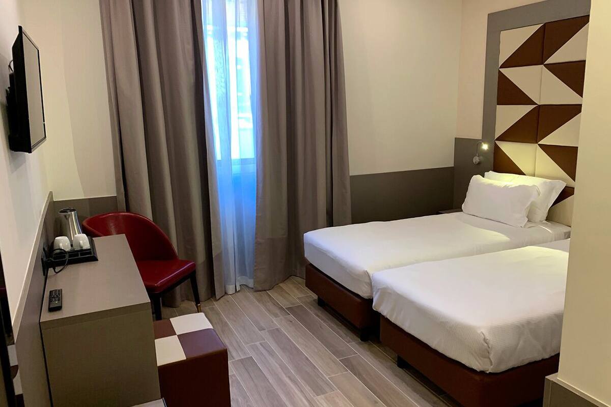 A hotel room with two beds, a desk with a chair, a TV, and a window with curtains.