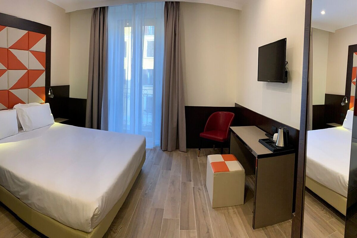 Quarto de hotel com uma cama grande, uma mesa, uma cadeira e uma televisão.