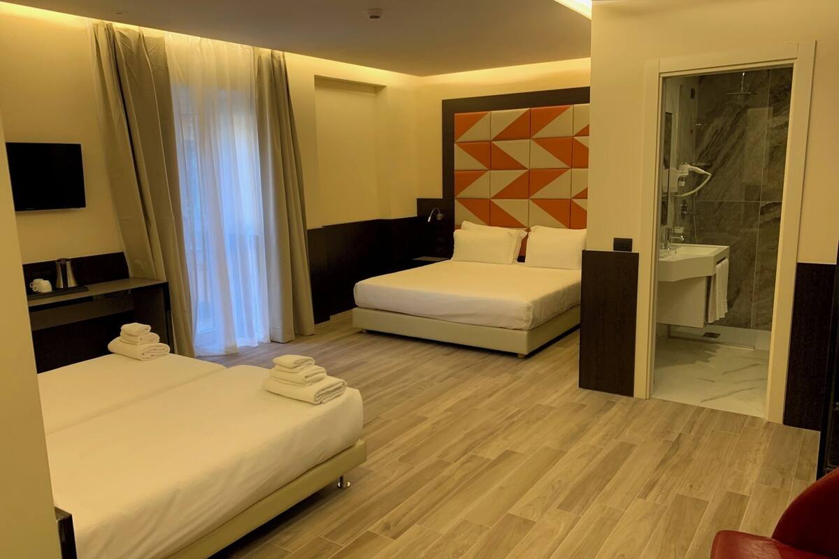 A hotel room with two beds, a shower, a sink, and a TV.
