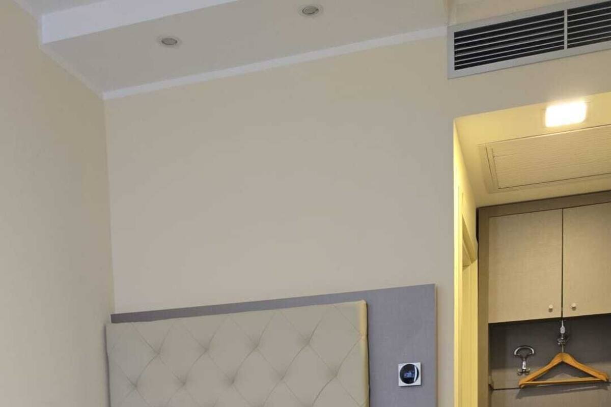 A hotel room with a large bed, a bedside table with a phone and a lamp, a wardrobe, and a shoe rack.