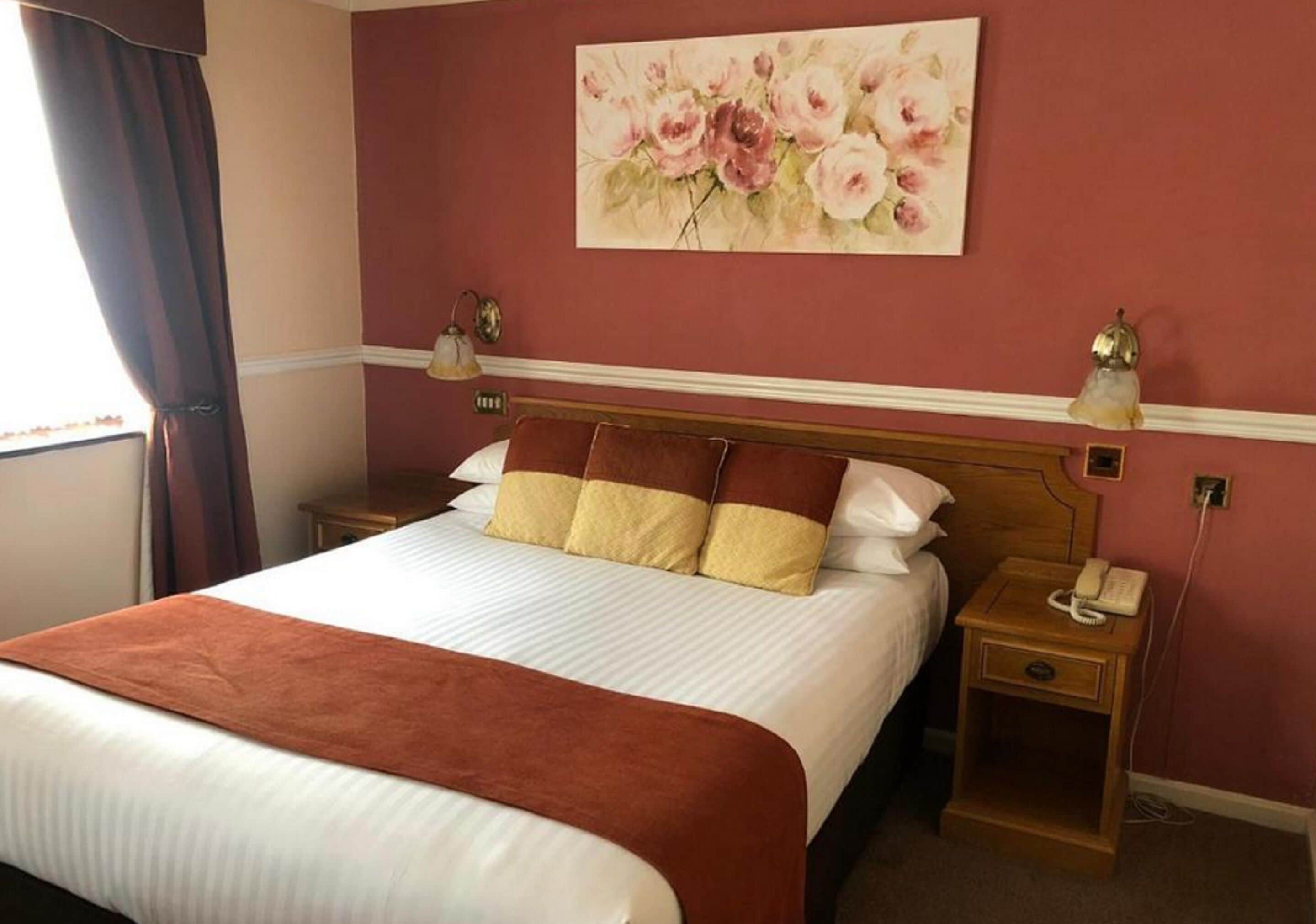 A hotel room with a large bed, two bedside tables, a telephone, and a floral painting on the wall.