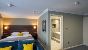 A hotel room with a bed, a blue sofa, a bathroom with a bathtub, and a shower. - Beaufort Park Hotel (Mold)