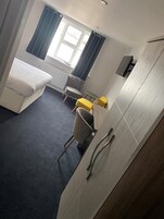 A hotel room with a bed, a chair, a small table, and a wardrobe.