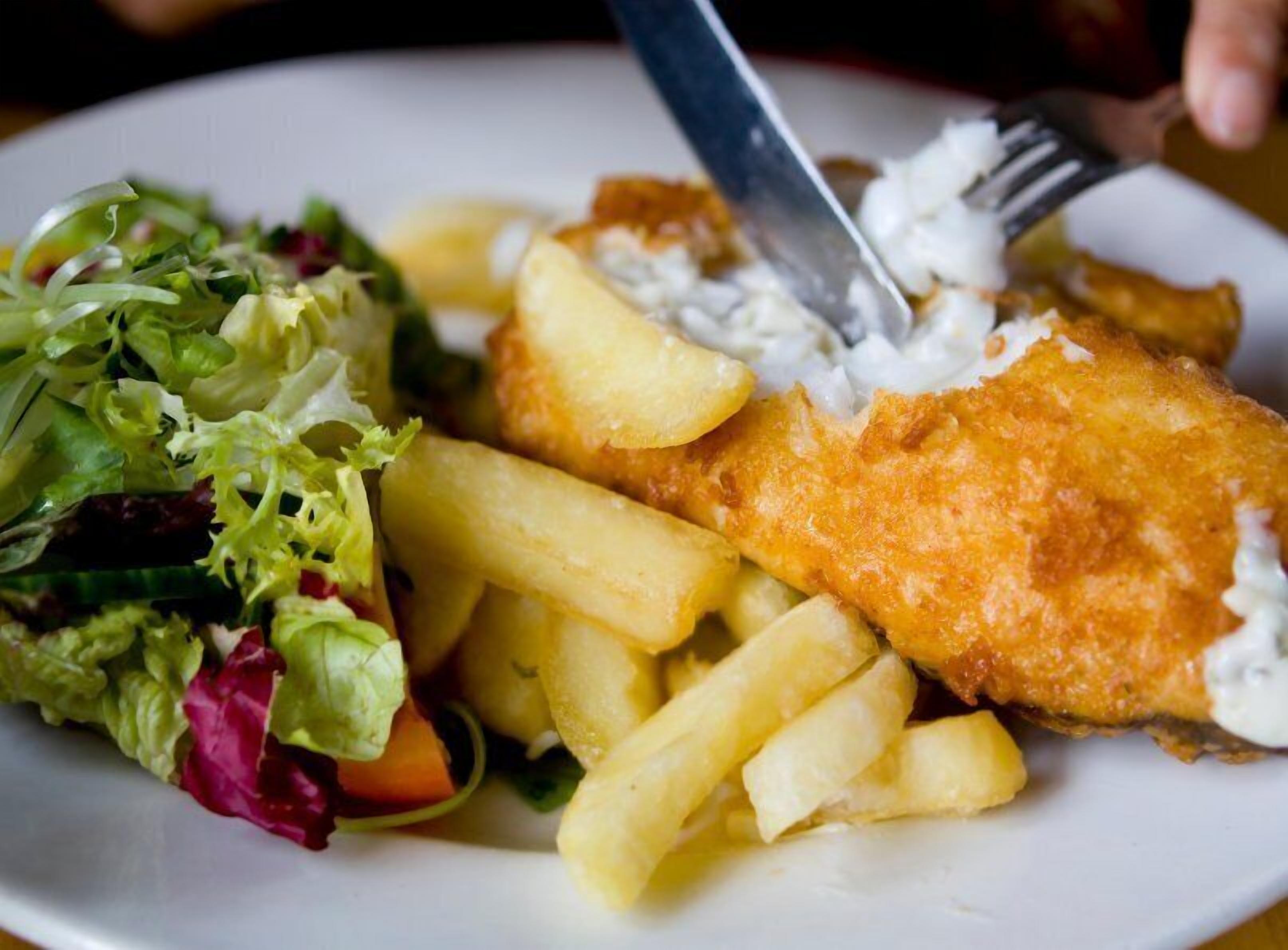 En tallrik med en panerad fiskfilé, pommes frites och en liten sallad.
