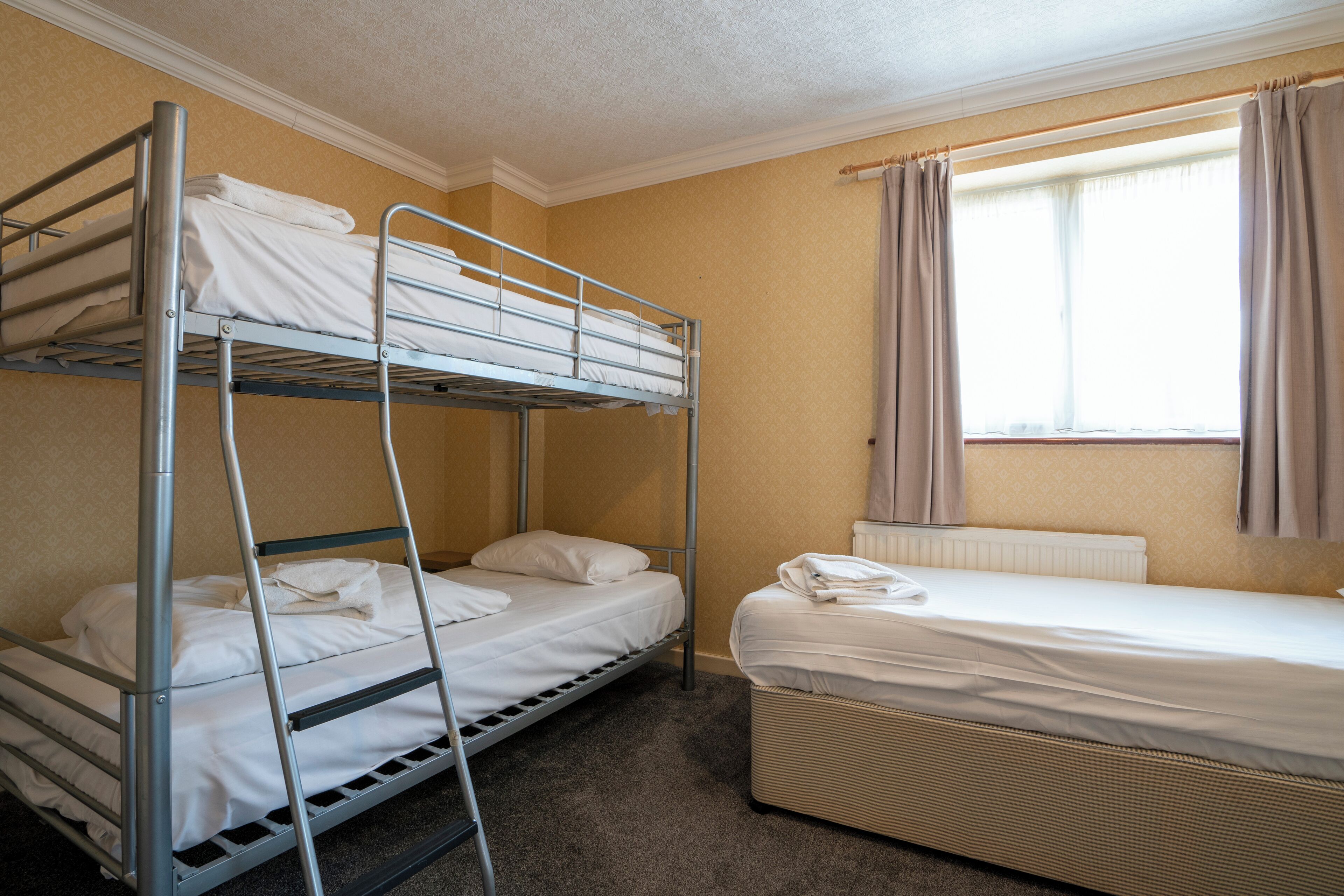 Habitación con literas, una cama individual y una ventana con cortinas.