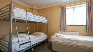 A bunk bed room with a single bed and a window with curtains.