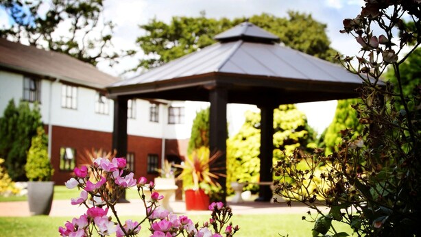A gazebo with a metal roof, surrounded by a well-maintained lawn and flowering plants. - Beaufort Park Hotel (Mold)