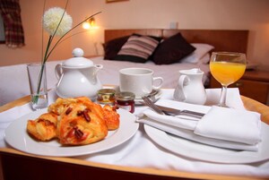 Bandeja de desayuno con cruasanes, un vaso de jugo de naranja, una taza, una jarrón y condimentos sobre una mesa de hotel.