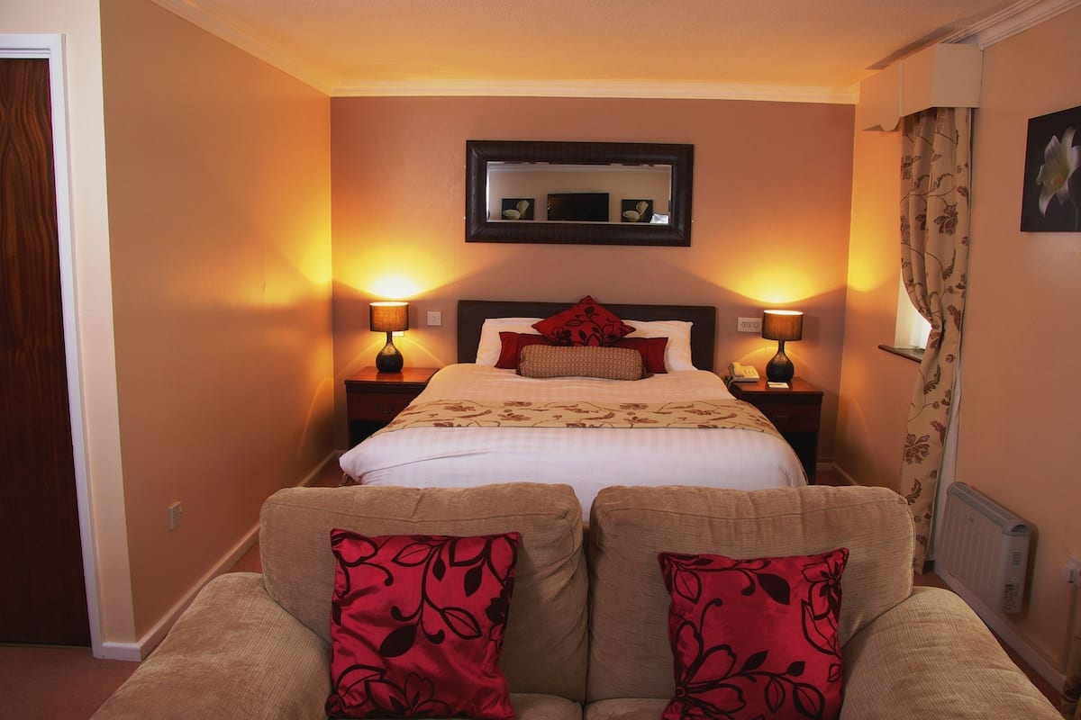 Quarto de hotel com cama, duas luminárias de cabeceira, mesa de cabeceira, espelho e janela com cortinas.