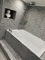 Un baño moderno con una bañera independiente, un cabezal de ducha y una escultura de mármol en la pared.