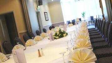 A long dining table set for a formal event with chairs, glassware, and a floral centerpiece.