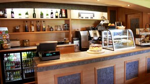 A hotel reception area with a counter, beverage dispensers, a coffee machine, and a display case with pastries. - Beaufort Park Hotel (Mold)