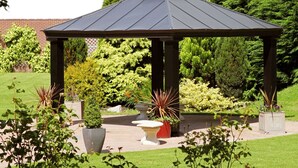 A gazebo with a dark roof and four supporting columns, surrounded by a variety of potted plants and shrubs in a landscaped garden. - Beaufort Park Hotel (Mold)