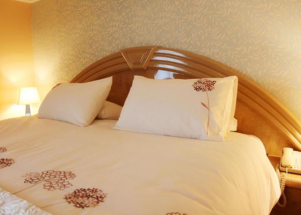 Een net opgemaakt bed met een bloemenbedekker, een houten hoofdbord en een bedtelefoon.
