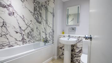 Un baño con pared de mármol, cabina de ducha de cristal, lavamanos pedestal y un inodoro.