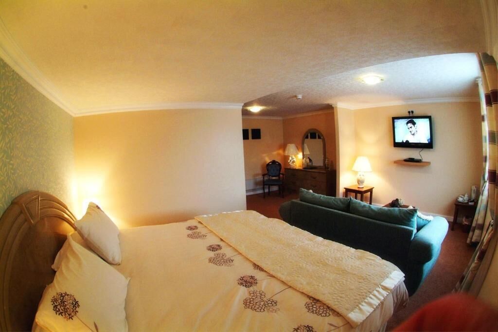 A hotel room with a bed, a green sofa, a television, and a desk with a lamp.