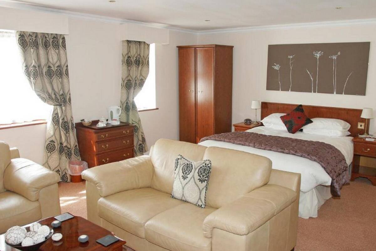 Quarto de hotel com uma cama, um guarda-roupa de madeira, um sofá bege, uma mesa de centro e um quadro na parede.